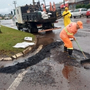 A imagem mostra dois homens trabalhando na pista danificada pela chuva e um caminhão estacionado. 